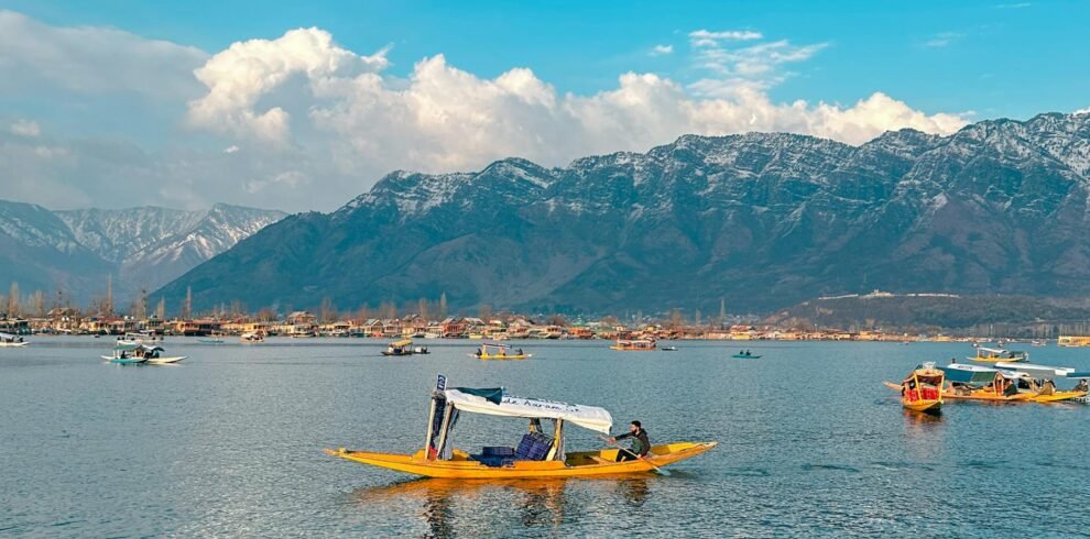 Shikara boats floating on Dal Lake with snow-capped Himalayan mountains in Srinagar, Kashmir under a vibrant blue sky