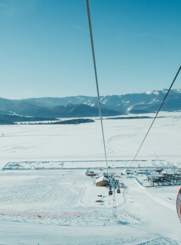 Red Gulmarg Gondola cabin gliding over snow-covered slopes in Kashmir with panoramic views of the Himalayas under a clear blue sky.