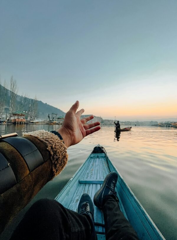 Traveler enjoying a peaceful Shikara ride on Dal Lake in Srinagar, Kashmir, at sunrise with reflections of mountains and boats on calm water.