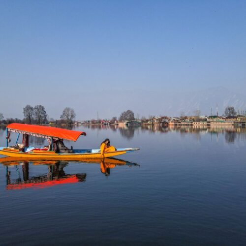 Traditional shikara gliding across Dal Lake in Srinagar with houseboats and the Zabarwan mountains in the background.