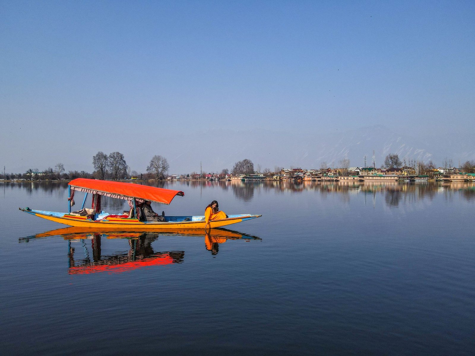 Traditional shikara gliding across Dal Lake in Srinagar with houseboats and the Zabarwan mountains in the background.