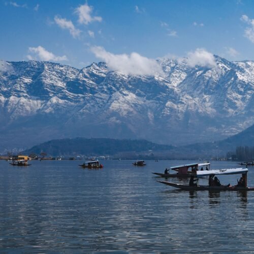 Traditional shikaras on Dal Lake with the snow-covered Zabarwan Mountains in Srinagar, Kashmir.