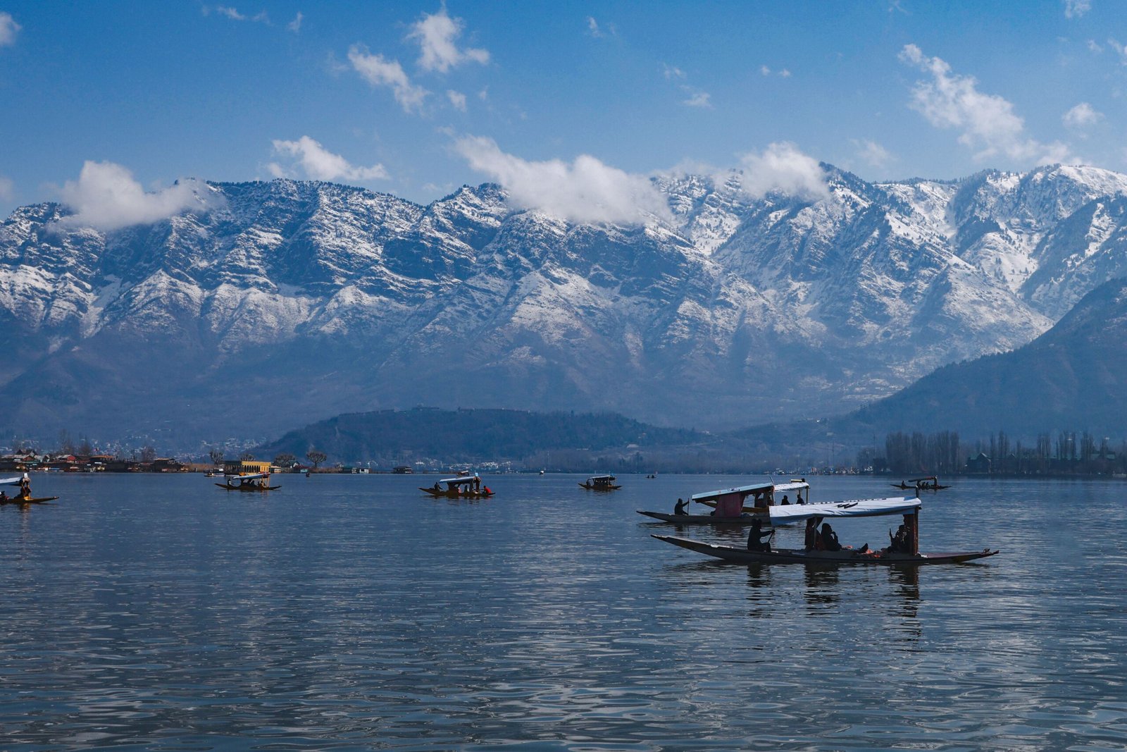 Traditional shikaras on Dal Lake with the snow-covered Zabarwan Mountains in Srinagar, Kashmir.